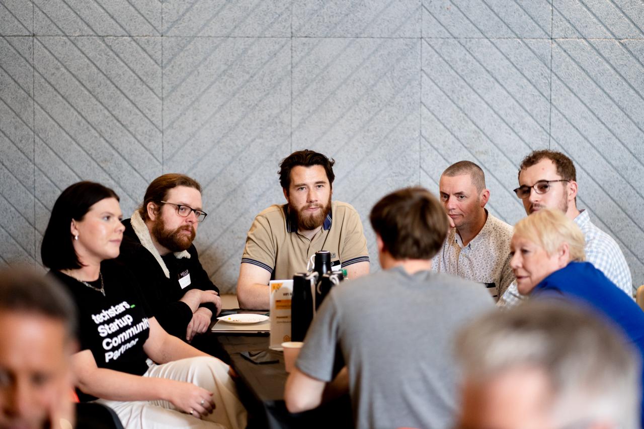 Six founders gathered around a table, listening